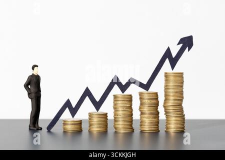Geschäftsmann mit Blick auf steigende Münzstapel und wachsende Diagrammpfeile, die nach oben zeigen, Konzept für Unternehmenswachstum und Investitionen Stockfoto