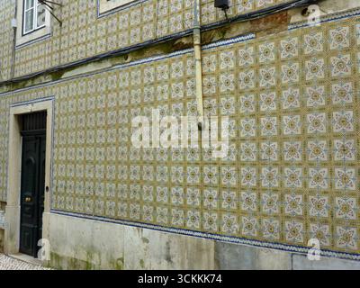 Dekorative Außenwand mit traditionellen portugiesischen Azulejos, mit komplexen geometrischen und floralen Mustern, hauptsächlich in Gelbtönen. Stockfoto