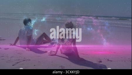 Sitzender Mann und Frau, die den Meereshorizont am Sandstrand betrachten, mit breitem Strohhut Stockfoto