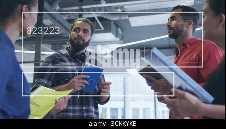Datenmann mit kariertem Hemd und Kopfhörern, der Notebook im Büro mit UI-Overlay hält Stockfoto