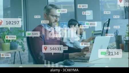 Tippkabel mit braunem Pullover auf silbernem Laptop im Großraumbüro mit Monitoren, schwimmenden Overlays Stockfoto