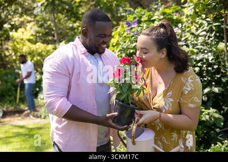 Diverse Paare mit schwarzem Topf mit roten Blüten und Freund Rasen im sonnigen Hinterhof Stockfoto