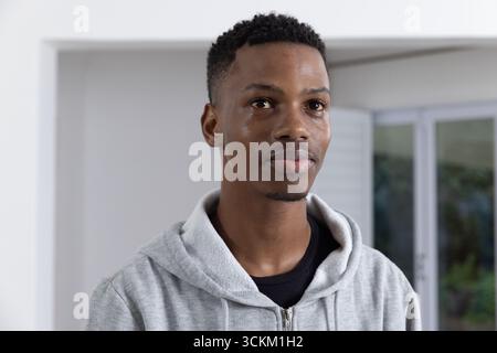 afroamerikanischer Mann in grauem Hoodie, der neben Fensterläden zu Hause steht und Grün zeigt Stockfoto