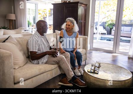 Diverse Seniorenpaare zur Überwachung des Blutdrucks im Wohnzimmer mit Digitalmonitor und Smartphone Stockfoto