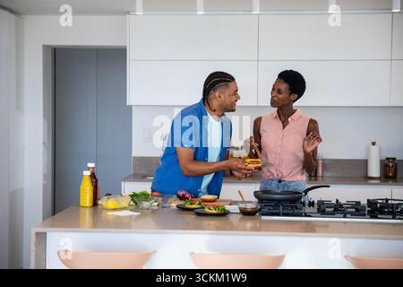 Diverse Freunde kochen Burger auf der Kücheninsel zu Hause mit Holzspachtel und Schneidebrett Stockfoto
