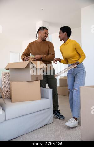 Diverse Paare, die Umzugskartons im Wohnzimmer auspacken, mit hölzernem Bilderrahmen und Glasgefäß Stockfoto