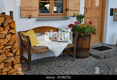 Rustikaler albayerischer Bauernhof mit Holzbank, traditionellem Brennholzhaufen und bunten Blumen im bayerischen Alpendorf Schwangau Stockfoto