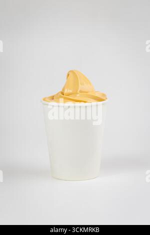Gelbes Mangosorbet wirbeln in Papierbecher auf weißem Hintergrund, minimalistisches Studio-Bild Stockfoto