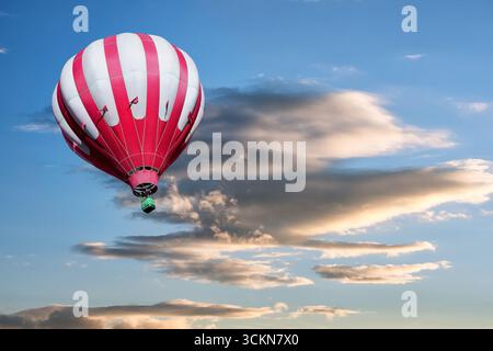 Rot-weißer Heißluftballon auf dem Hintergrund des hellen rosigen Sonnenuntergangs. Stockfoto