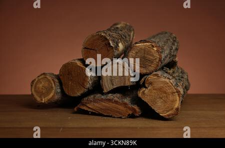Haufen von geschnittenem Brennholz auf Holztisch vor braunem Hintergrund, Nahaufnahme Stockfoto