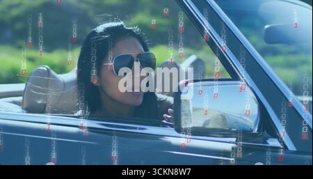 Indische Frau mit Sonnenbrille, die Cabrio auf Landstraßen fährt, mit Binärcode-Overlay Stockfoto