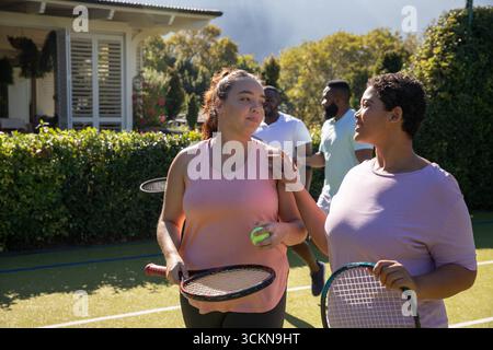 Verschiedene Freunde laufen, plaudern auf dem Rasen-Tennisplatz mit Schlägern, Ball und Leinen, Kopierraum Stockfoto
