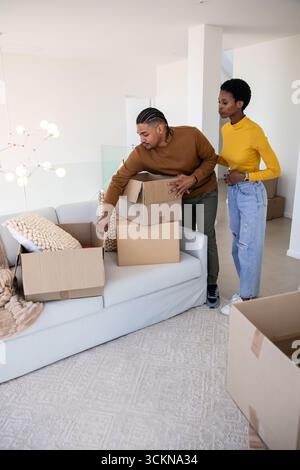 Diverse Paare, die Umzugskartons auf einem modernen Sofa im Wohnzimmer mit strukturiertem Überwurfkissen auspacken Stockfoto