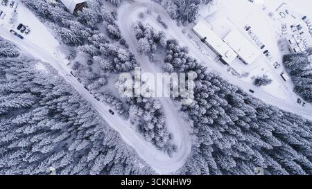 Blick von oben nach unten auf die Straße, die durch den Wald in der Winterschneelandschaft führt. Drohne in der schneebedeckten Berglandschaft Stockfoto
