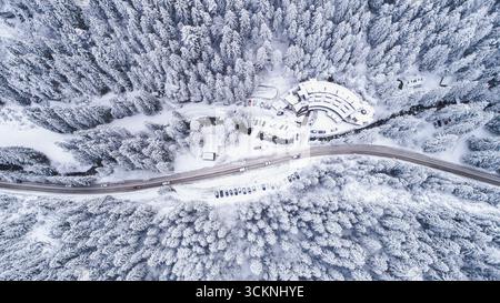 Blick von oben nach unten auf die Straße, die durch den Wald in der Winterschneelandschaft führt. Drohne in der schneebedeckten Berglandschaft Stockfoto