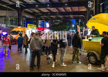 Ein lebhafter Markt im Freien bei Nacht mit Food Trucks, Straßenverkäufern und hektischen Menschenmassen, die die lebhafte Atmosphäre unter Stadtlichtern genießen, Opt OV Stockfoto