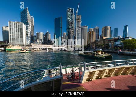 Sydneys Stadtbild mit einer lebendigen modernen Skyline mit hohen Gebäuden, Aktivitäten am Wasser und dynamischen Bootsbewegungen unter einem klaren blauen Himmel, Stockfoto