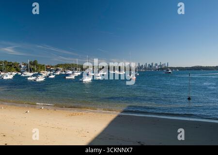 Schöner Hafen mit angedockten Segelbooten, ruhigem Wasser, sonnigen Bedingungen und einer Skyline der Stadt in der Ferne. Ideal zur Illustration von Gelassenheit, ur Stockfoto