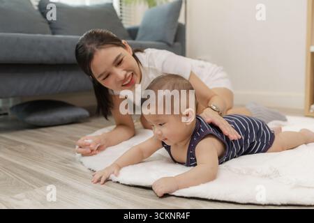 Ein Baby genießt die Bauchzeit auf einer weichen Matte, während die Mutter nah bleibt und es mit einem warmen Lächeln ermutigt. Dieser zärtliche Moment hebt frühe Entwicklungskräfte hervor Stockfoto