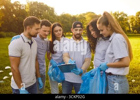 Gruppe junger Freinds, Team-Erwachsene, die sich versammeln, sich den Plan ansehen, blaue Taschen halten, Handschuhe halten Stockfoto