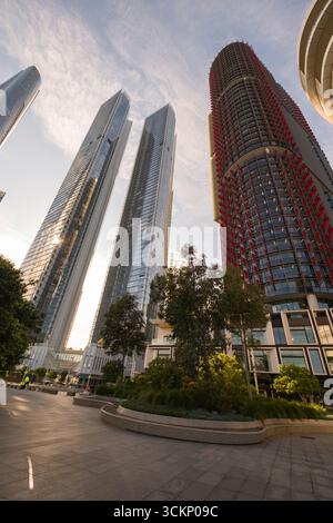 Hohe, moderne Glasgebäude reflektieren das Sonnenlicht, umgeben von üppigem Grün in einer urbanen Landschaft. Die pulsierende Architektur ist ein wunderschöner Kontrast Stockfoto