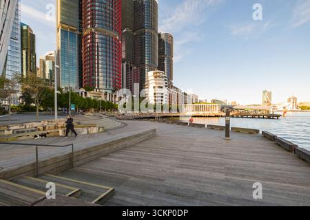 Ein malerischer urbaner Fußweg am Hafen mit moderner Architektur, Hochhäusern, ruhiger Uferpromenade und Freizeiteinrichtungen, Barangaroo, Sydney Stockfoto