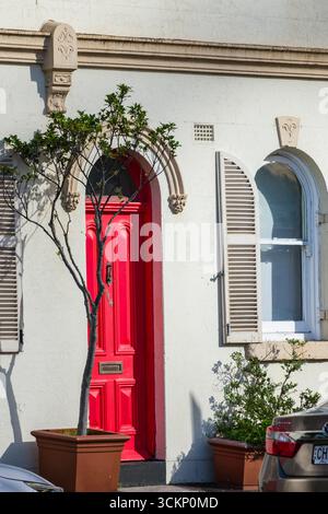 Eine hellrote Tür ziert die Fassade eines Stuckgebäudes, ergänzt durch Bogenfenster und Topfpflanzen, Sydney Stockfoto