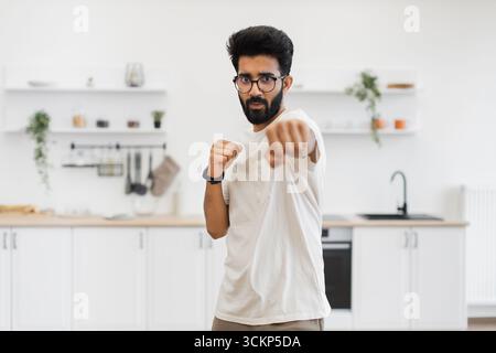 Mann, der mit Entschlossenheit Boxtechniken in der Küchenumgebung übt Stockfoto