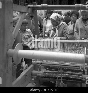 Eine Demonstration traditioneller Handwerkskunst während der Feierlichkeiten zum Stadttag in Sloviansk, 1988. Eine ältere Handwerkerin in einem traditionellen Kopftuch zeigt Kindern und Erwachsenen die Kunst des Webens auf einem alten Holzwebstuhl. Diese Szene spiegelt das starke Interesse an Volkskultur und nationalen Traditionen wider, das für die Perestroika-Ära charakteristisch war und die lebenswichtige Verbindung zwischen den Generationen und die Erhaltung des historischen Erbes in einer Zeit großer sozialer Veränderungen symbolisiert Stockfoto