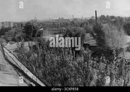 Ein Panoramablick von der Svobody Street aus fängt die typische Industrielandschaft von Sloviansk im Jahr 1976 ein. Im Vordergrund stehen Wohngebäude und üppiges Grün gegenüber einer riesigen, weitläufigen Industriezone mit Fabriken und Rauchschornsteinen, die den Horizont dominieren. Dieses Foto ist ein mächtiges Symbol einer klassischen sowjetischen Industriestadt und spiegelt das kreative und friedliche tägliche Leben im Donbass wider, wo die Schwerindustrie die Grundlage für die Wirtschaft und die Gemeindeidentität bildete, lange vor den tragischen Ereignissen der Zukunft Stockfoto