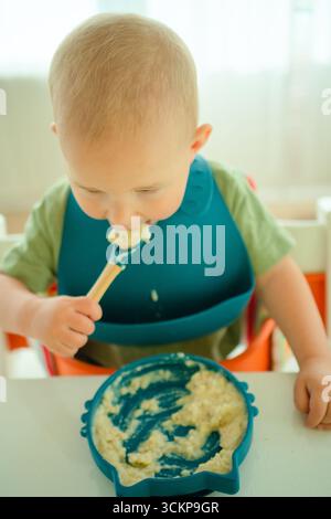 Aus der Vogelperspektive kann das Kleinkind nahrhaften Haferbrei unabhängig essen und wichtige Meilensteine beim Absetzen und Füttern von oben erfassen. Stockfoto
