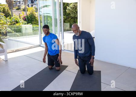 afroamerikanischer Vater und Sohn kniend auf schwarzen Yogamatten auf der Terrasse in Sportbekleidung Stockfoto