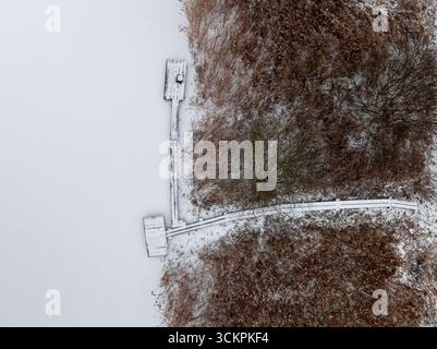 Aus der Vogelperspektive auf die schneebedeckte Brücke über einen gefrorenen See. Sport auf dem gefrorenen See. Stockfoto