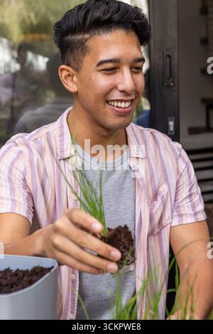 Mann, der grüne Triebe mit Erdklumpen in einen grauen Pflanztopf auf einer Terrasse mit Ablagefläche vergossen hat Stockfoto