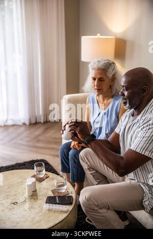 Seniorenpaar sitzt auf dem Sofa, öffnet die Pille Flasche und sortiert wöchentliche Pille Organizer zu Hause Stockfoto
