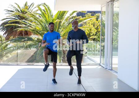 afroamerikanischer Vater und Sohn, der in Sportbekleidung wechselnde Knie-Lifte auf dem Balkon durchführen Stockfoto