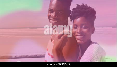 Ein lächelndes romantisches Paar mit gestreiften Oberteilen, die nahe am Sandstrand stehen, traumhafte Pastellüberzüge Stockfoto
