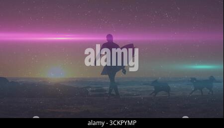 Walking Silhouette Mann im Taucheranzug mit Surfbrett am Sonnenuntergang Strand, mit zwei Hunden, die auf Sand laufen Stockfoto