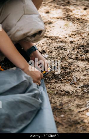 Nahaufnahme weiblicher Hände, die während des Campings ein Zelt mit Gurten am Boden befestigen Stockfoto