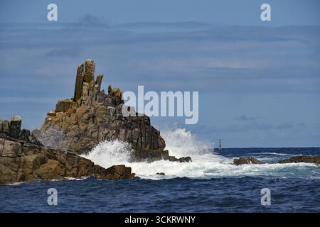 Raues Meer mit Wellen, die unter blauem Himmel gegen Felsen krachen, Scilly-Inseln, Cornwall, Großbritannien Stockfoto