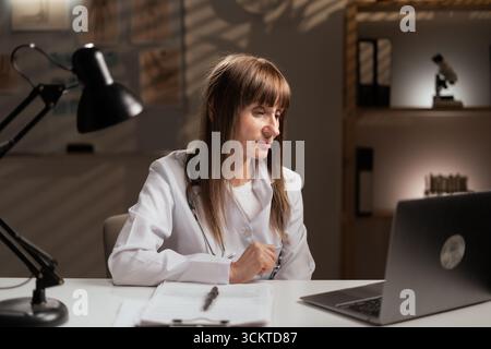 Leitende Ärztin im Krankenhaus, die spät in Telehealth oder Forschung arbeitet. Arzt liest Gesundheitsinformationen. Kopierbereich Stockfoto