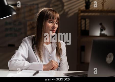 Leitende Ärztin im Krankenhaus, die spät in Telehealth oder Forschung arbeitet. Arzt liest Gesundheitsinformationen. Kopierbereich Stockfoto