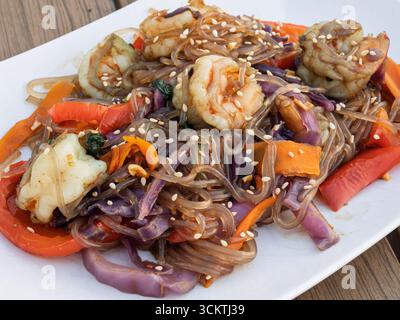 Eine lebendige und köstliche Nahaufnahme einer Garnelenpfanne mit Reisnudeln und frischem Gemüse auf einem weißen Teller. Stockfoto
