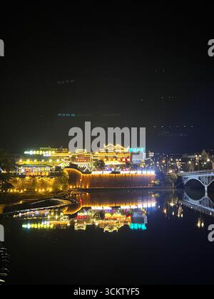 Zhangjiajie bei Nacht – Neonreflexionen tanzen auf dem Fluss unter den leuchtenden Lichtern der Stadt. Stockfoto