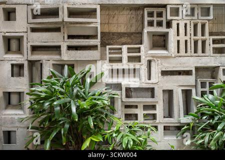 Ein innovatives architektonisches Wanddesign mit geometrischem Betonblockmuster, ergänzt durch üppiges grünes Laub. Stockfoto