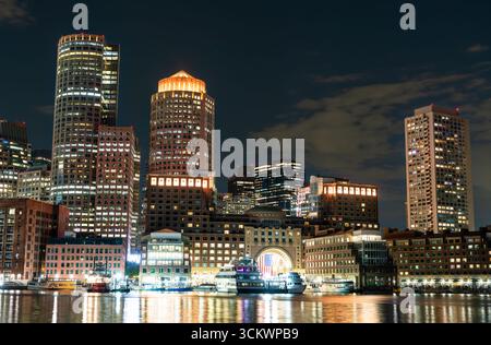 Die beleuchtete Skyline der Innenstadt von Boston, darunter das Boston Harbor Hotel mit seinem berühmten Bogen, der nachts auf dem Wasser des Hafens reflektiert. Massachusetts, Usa Stockfoto