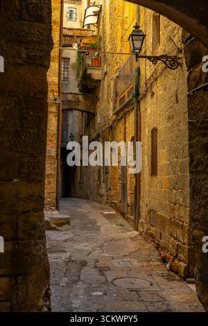 Pitiglianos historischer Charme erstrahlt durch eine enge kopfsteingepflasterte Gasse, flankiert von Steinhäusern und beleuchtet von einer alten Straßenlaterne Stockfoto