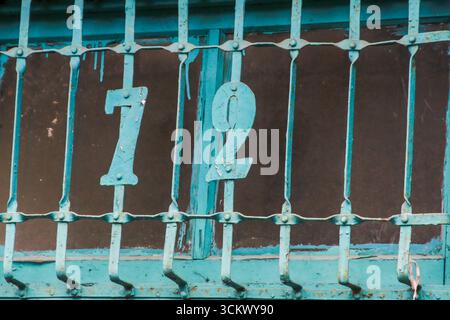 Ein blaues eisernes Fenster mit der Nummer 72 ziert ein altes Haus im Xian Guang Military Kindred Village Cultural Park in Taoyuan City, Taiwan, mit Weinwein Stockfoto