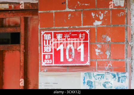 Taoyuan City, Taiwan - 01. Juni 2012: Ein rot-weißes Vintage-Gebäude mit der Nummer 101, das an einer verwitterten Ziegelwand mit abblätternder Farbe angebracht ist. Xian Guan Stockfoto