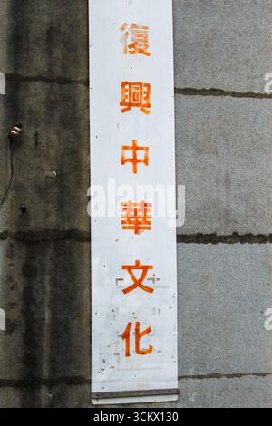 Taoyuan City, Taiwan - 01. Juni 2012: Nahaufnahme eines verwitterten weißen Schildes mit orangen chinesischen Schriftzeichen auf einer rauen Betonwand. Xian Guang Stockfoto